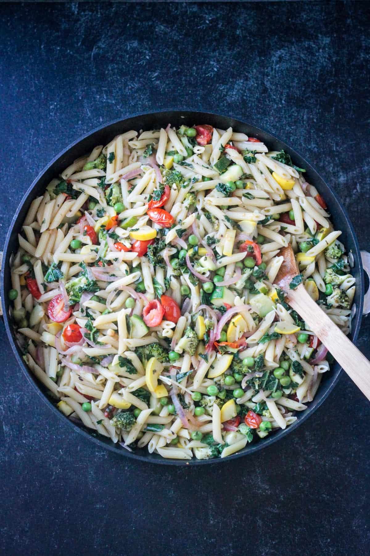 Wooden spoon stirring a skillet of pasta and veggies.