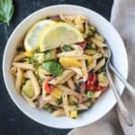 Vegan pasta primavera in a white bowl garnished with two lemon wedges.