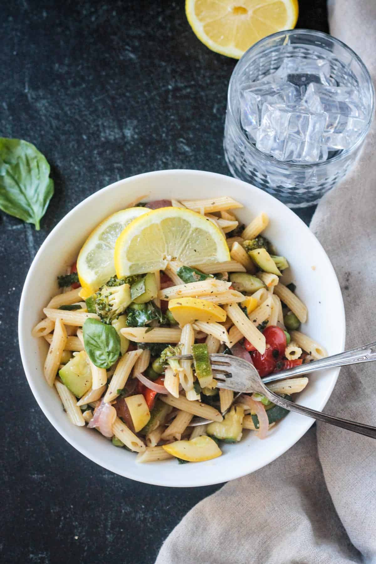 Bite of pasta primavera on a fork in a bowl.