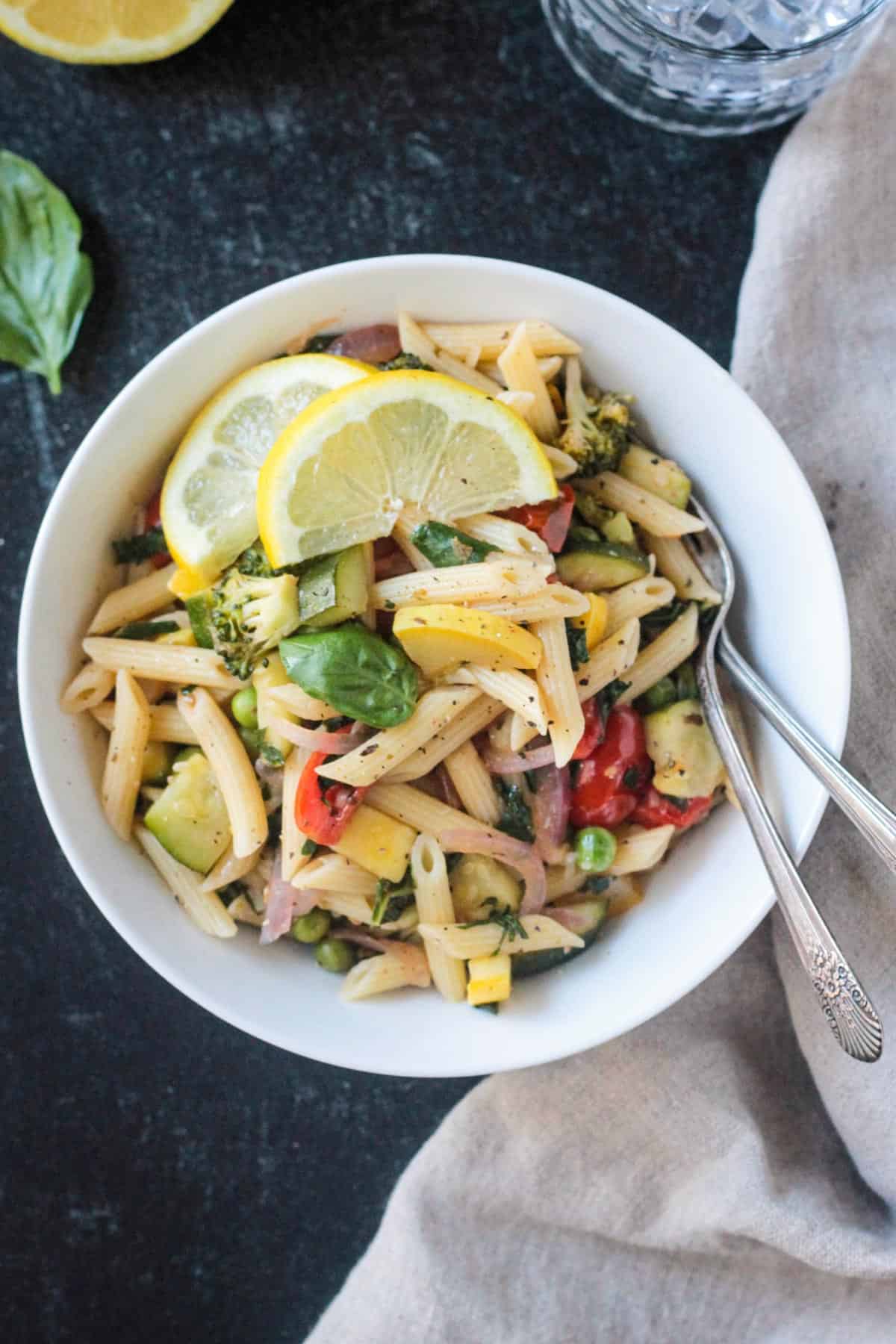 Vegan pasta primavera in a white bowl garnished with two lemon wedges.