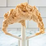 Paddle attachment from an electric stand mixer standing on end and covered in peanut butter frosting.