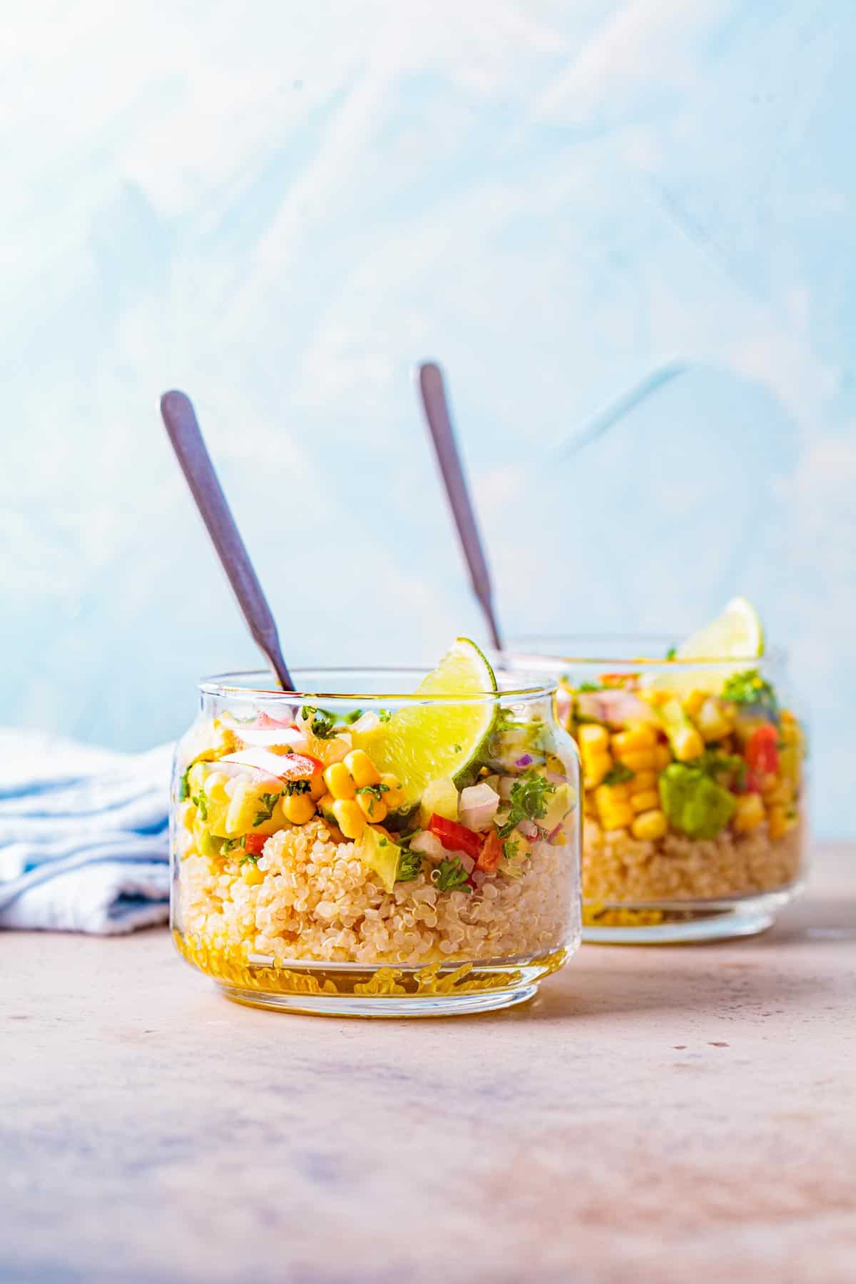 Two small jars of quinoa salad with a fork sticking out of each one.