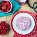 One heart shaped vegan raspberry cheesecake tart on a white and red plate.