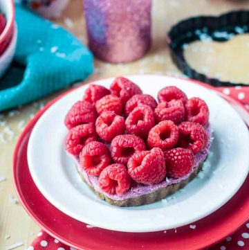 Raspberry Vegan Cheesecake in a heart shaped tart pan topped with fresh raspberries.
