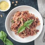 Fettuccine noodles with vegan bolognese garnished with fresh basil leaves.