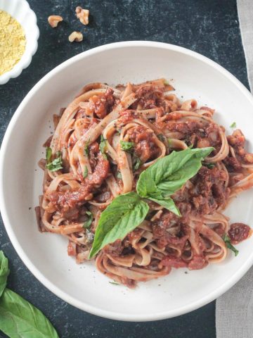 Fettuccine noodles with vegan bolognese garnished with fresh basil leaves.