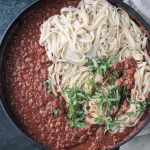 Chickpea walnut bolognese in a skillet with fettuccine noodles and fresh basil.