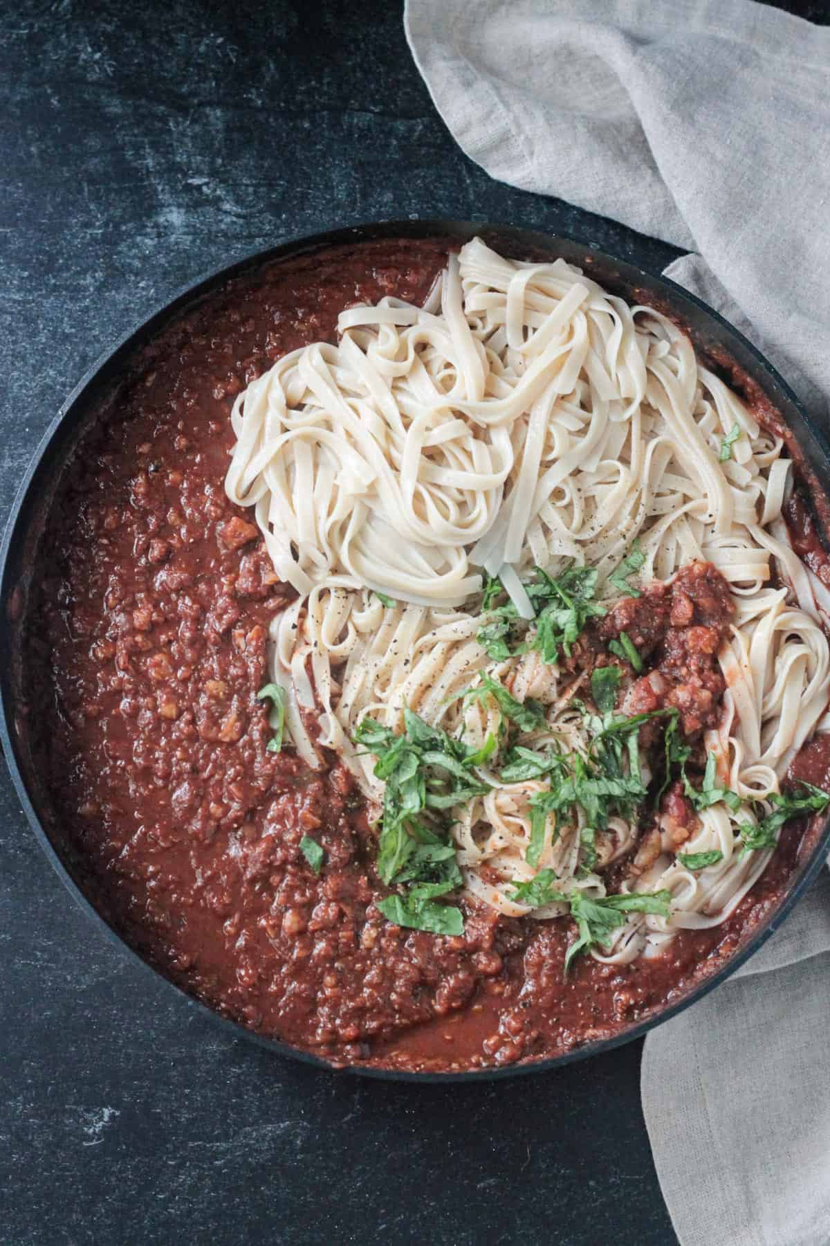 Chickpea walnut bolognese in a skillet with fettuccine noodles and fresh basil. 