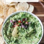 Guacamole dip in a bowl on a tray with a pile of tortilla chips.