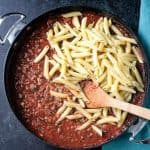 Penne noodles being added to a skillet of red sauce.