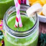 Two glasses full of green smoothie next to a bowl of sliced bananas.