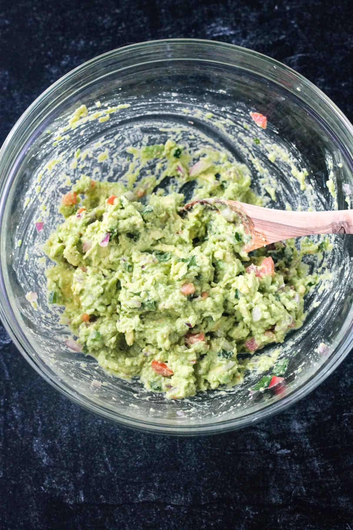 Ingredients mixed into guacamole in a glass bowl.