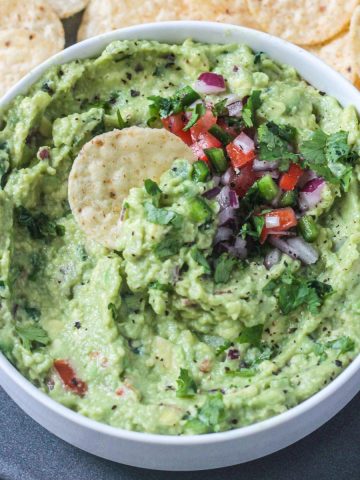 One tortilla chip dipped in a bowl of guacamole.