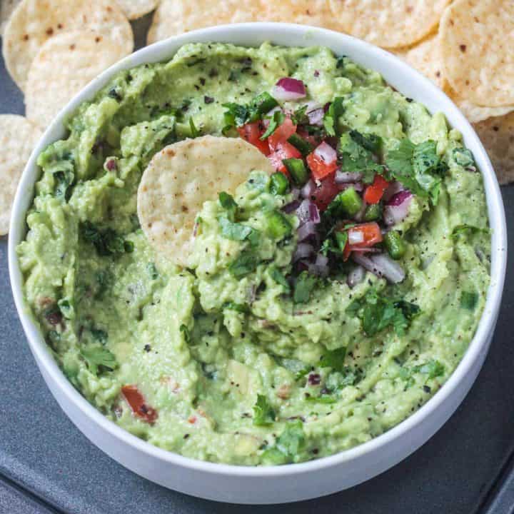 One tortilla chip dipped in a bowl of guacamole.