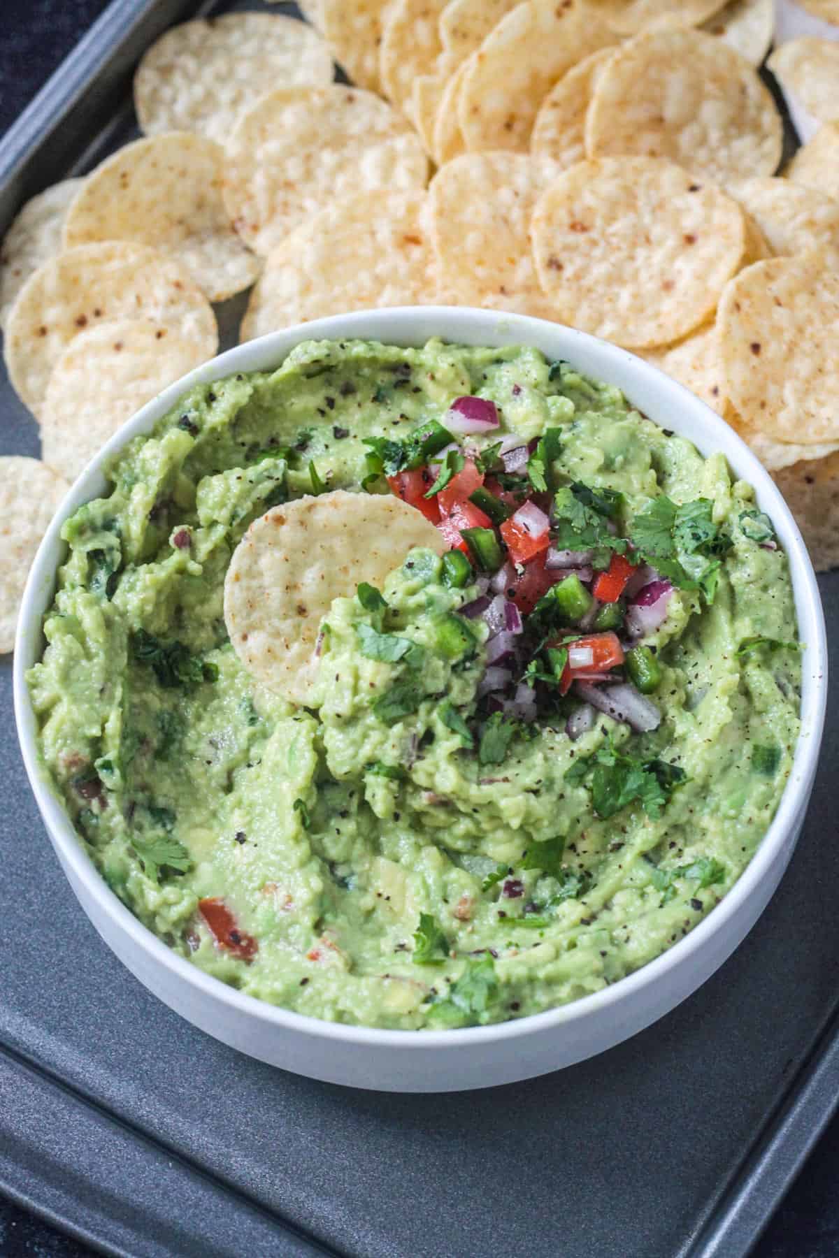 One tortilla chip dipped in a bowl of guacamole.