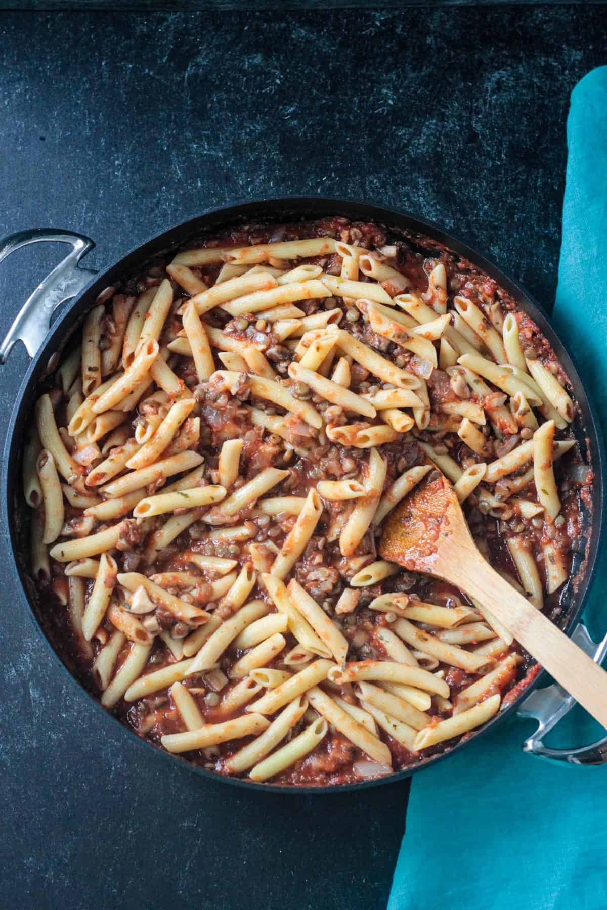 Penne noodles mixed in a skillet full of pasta sauce.