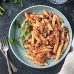 Penne with lentil mushroom lentil bolognese plated on a blue dish.