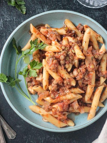 Penne with lentil mushroom lentil bolognese plated on a blue dish.