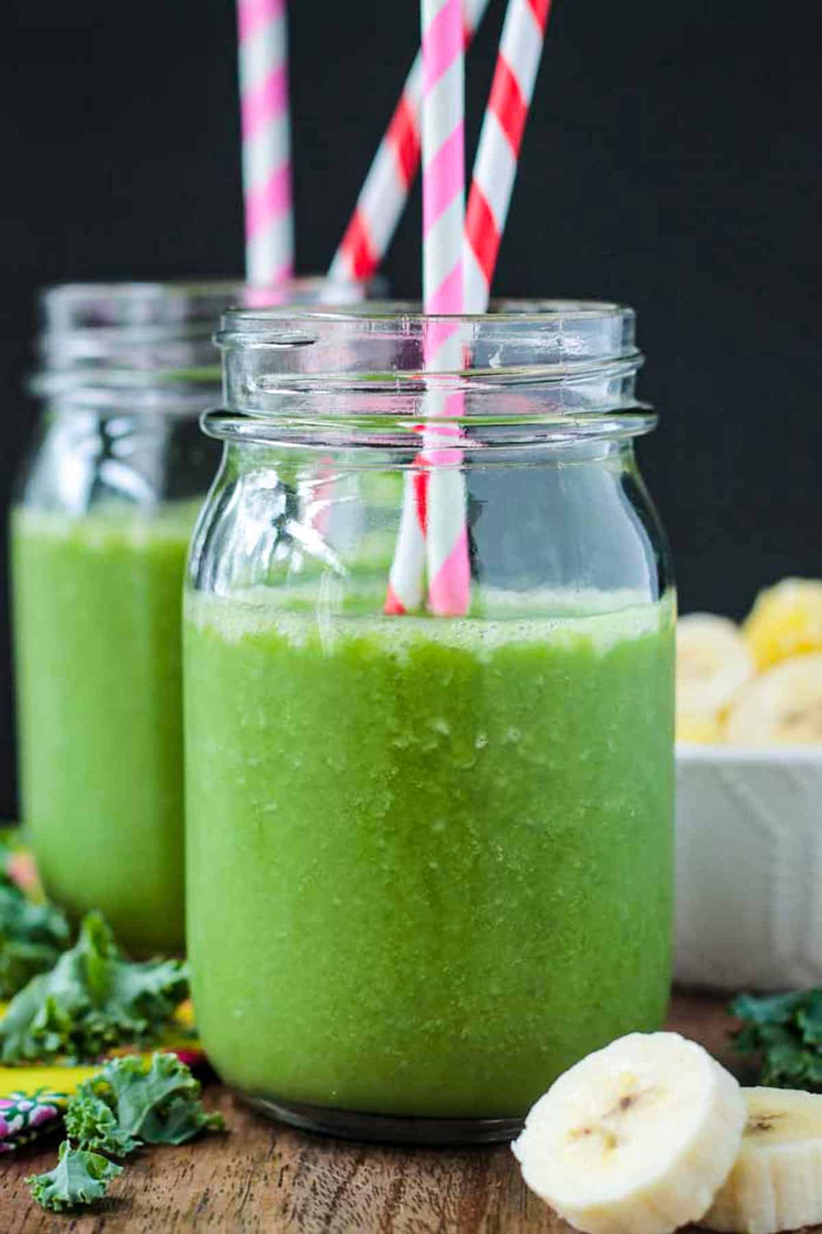 Pineapple Spinach Smoothie in a mason jar with two striped paper straws.