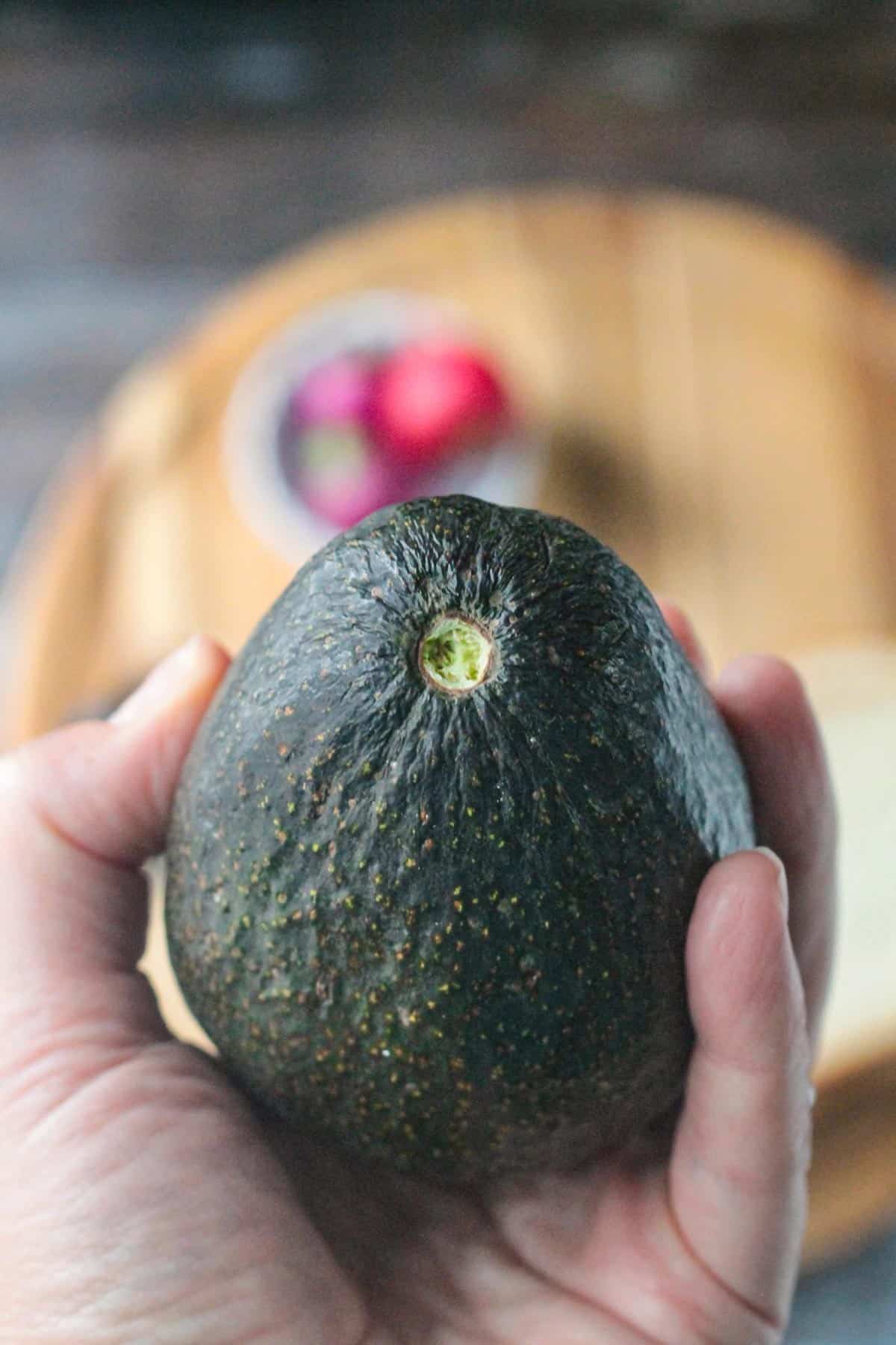 Hand holding a ripe avocado with the stem cap removed showing the green color underneath.