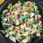 Salad with greens, vegetables, tofu, and walnuts in a black bowl.