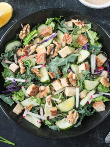 Salad with greens, vegetables, tofu, and walnuts in a black bowl.