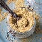 Small metal spoon in a jar of vegan parmesan cheese.