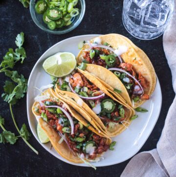 Three BBQ Jackfruit Tacos in corn tortillas on a plate with a lime wedge.