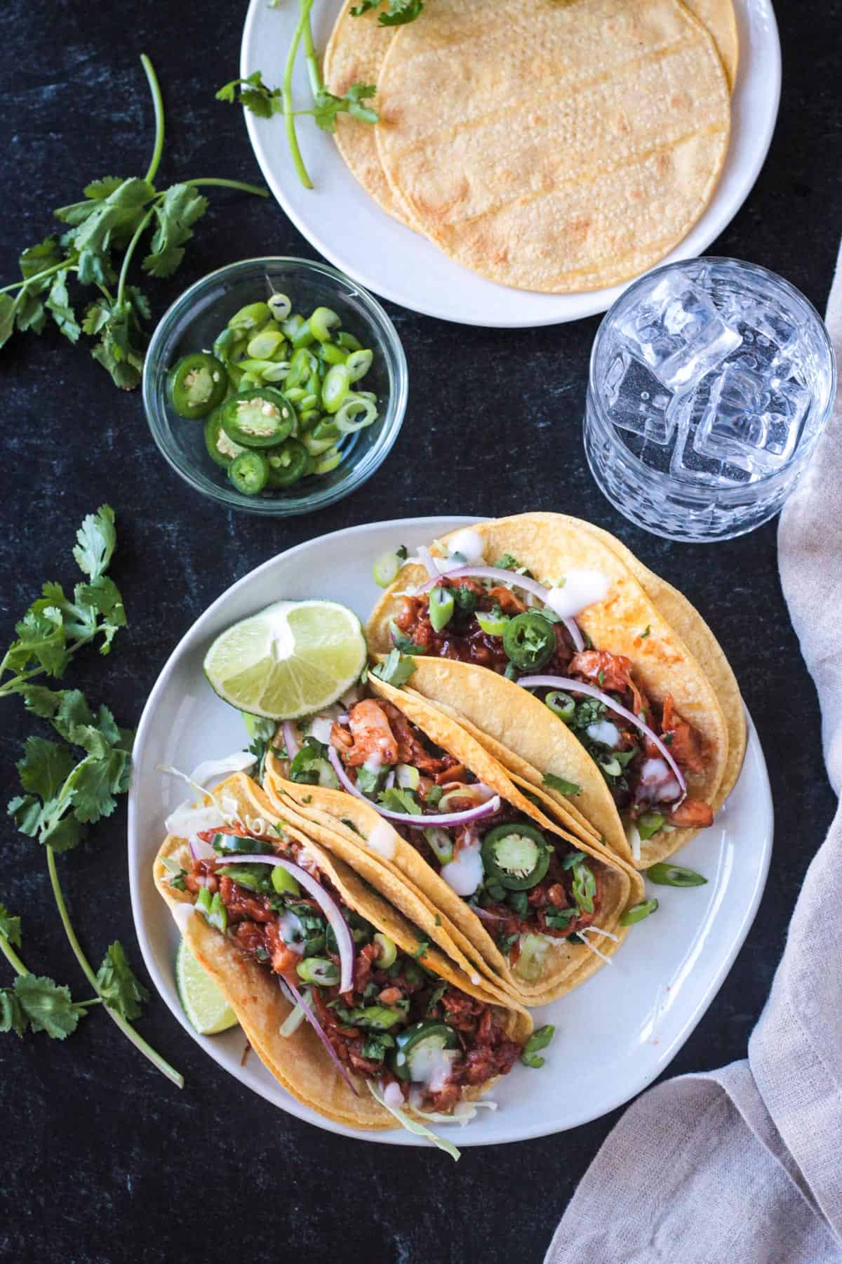 Three BBQ Jackfruit Tacos in corn tortillas on a plate with a lime wedge.