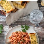 Plate of pasta with garlic bread in front of a basket full of more bread slices.