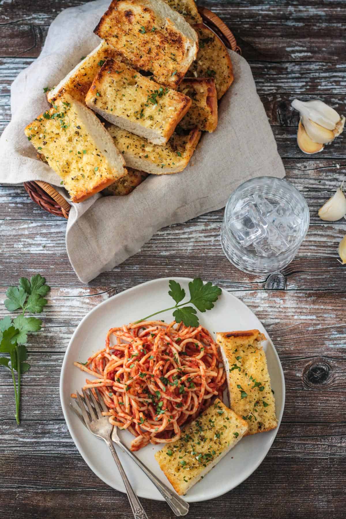 Plate of pasta with garlic bread in front of a basket full of more bread slices.