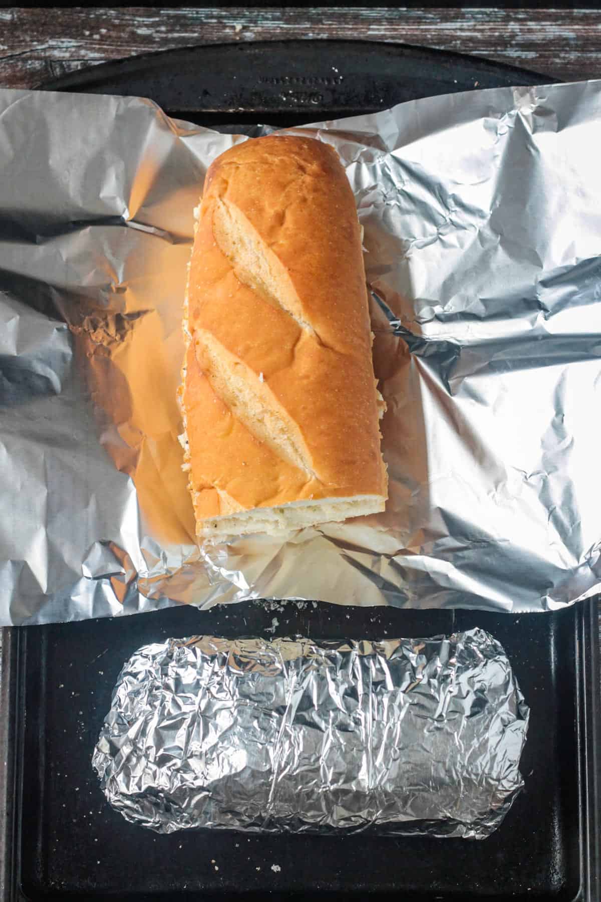 Wrapping garlic bread halves in foil to prepare for baking.