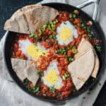 Vegan Shakshuka in a skillet with slices of pita dunked in the sauce.