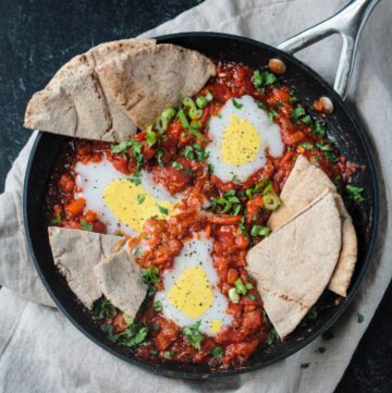 Vegan Shakshuka in a skillet with slices of pita dunked in the sauce.