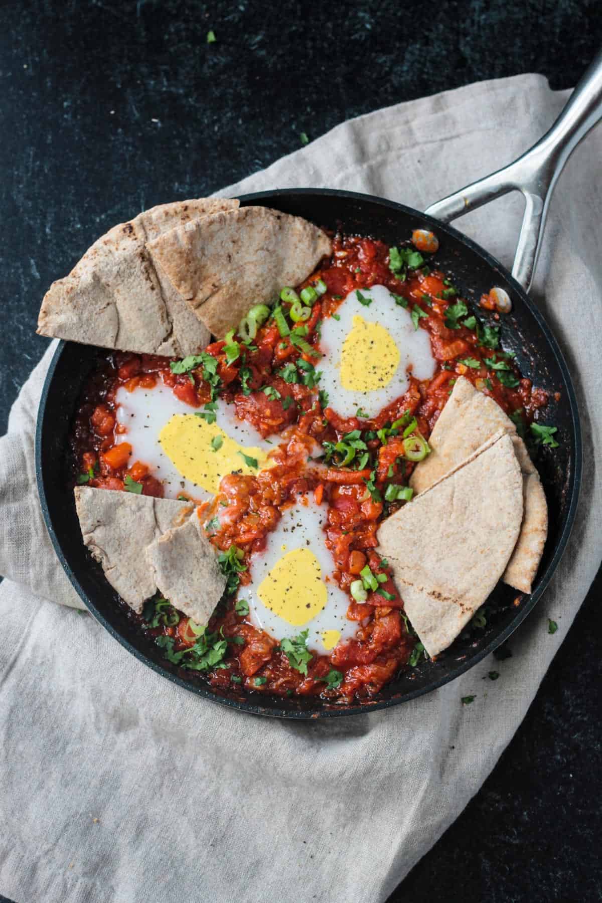 Vegan Shakshuka in a skillet with slices of pita dunked in the sauce.