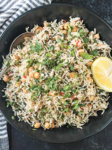 Spinach rice and chickpeas in a black serving bowl topped with a lemon wedge.