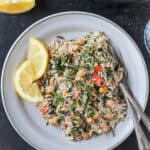 Rice with spinach and chickpeas on a gray plate with lemon wedges and two forks.