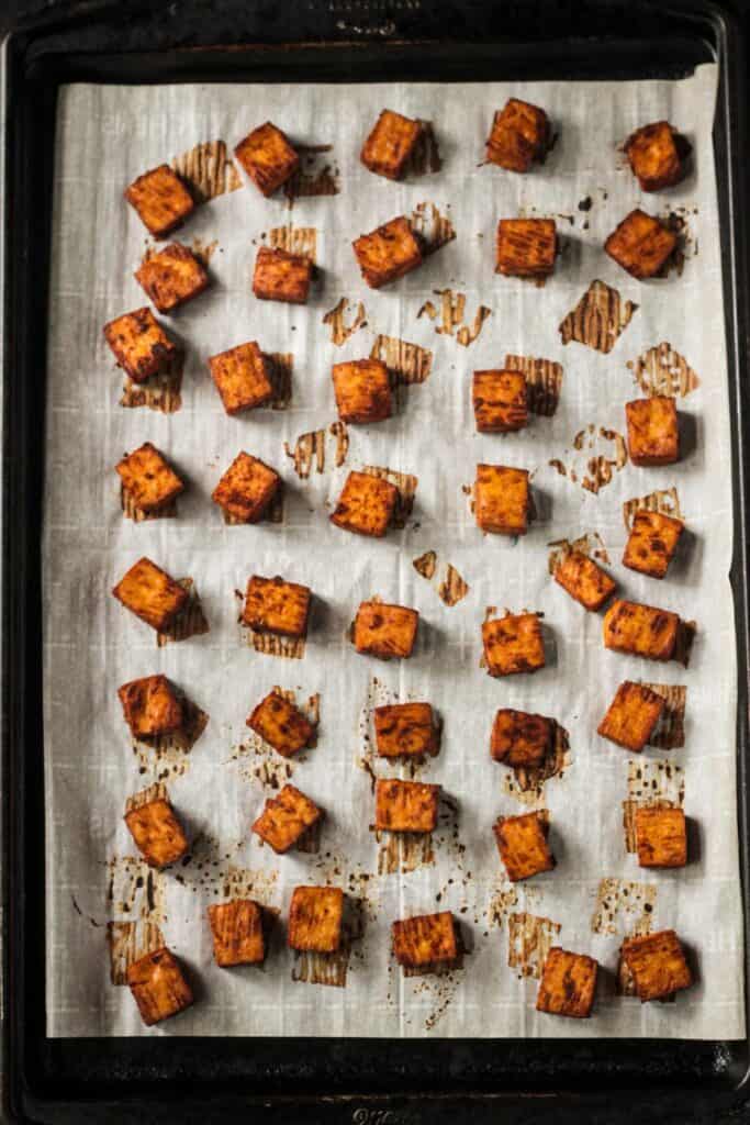 Cubes of baked tofu on a parchment lined baking sheet.
