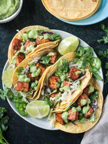 Four tofu tacos topped with avocado sauce on a plate.