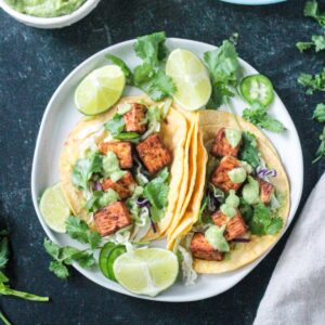 Two tacos filled with baked tofu, shredded cabbage, cilantro, and avocado sauce.