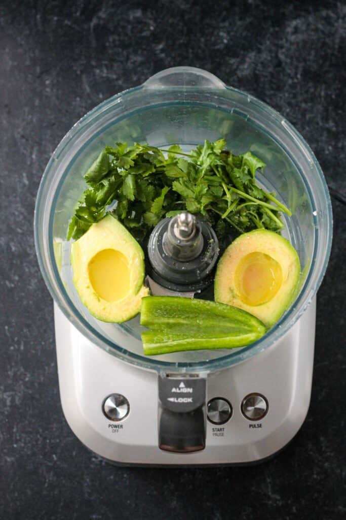 Avocado, jalapeño, cilantro, and lime juice in the bowl of a food processor.