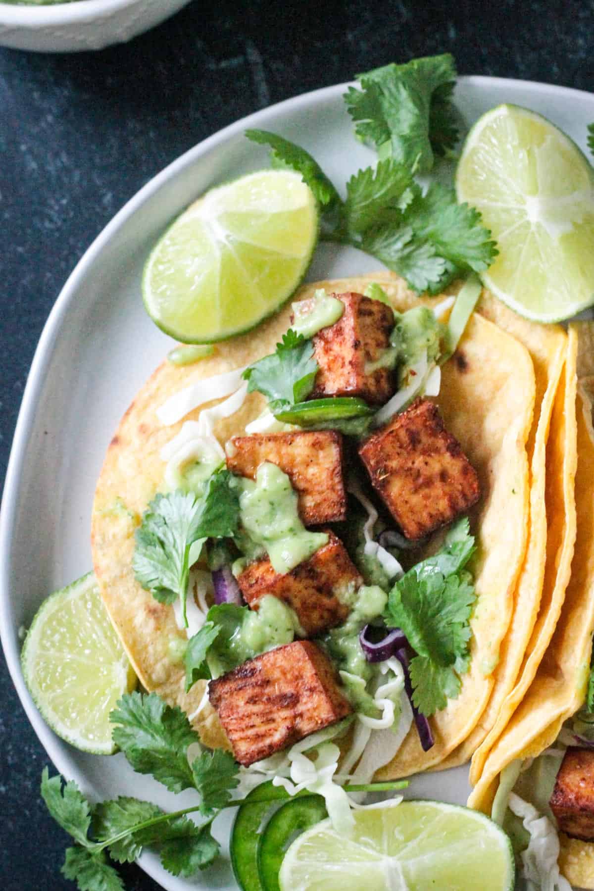 Five cubes of marinated baked tofu in a corn tortilla and topped with avocado lime sauce.