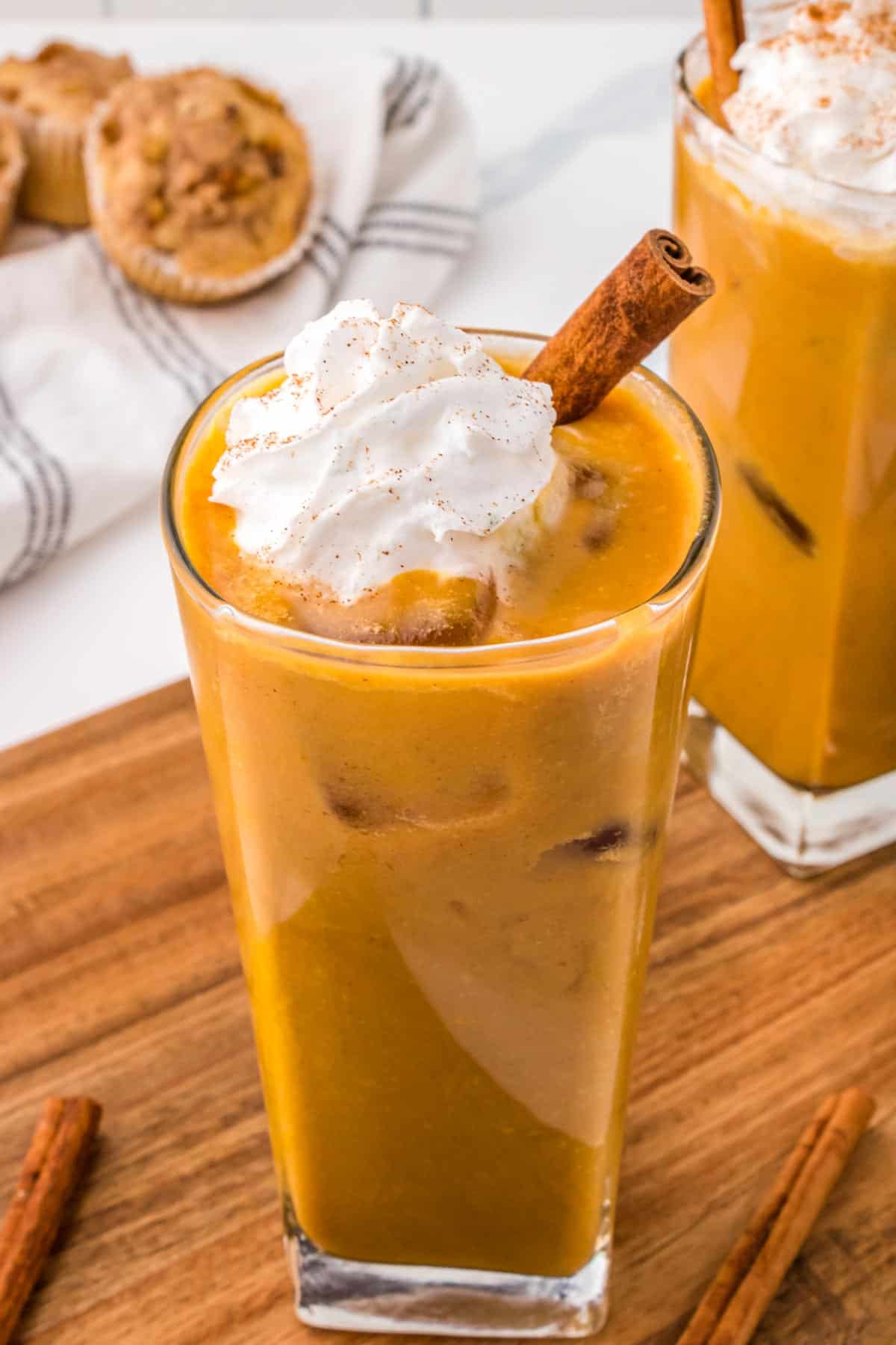 Pumpkin spiced iced latte in a glass topped with whipped cream and a cinnamon stick.