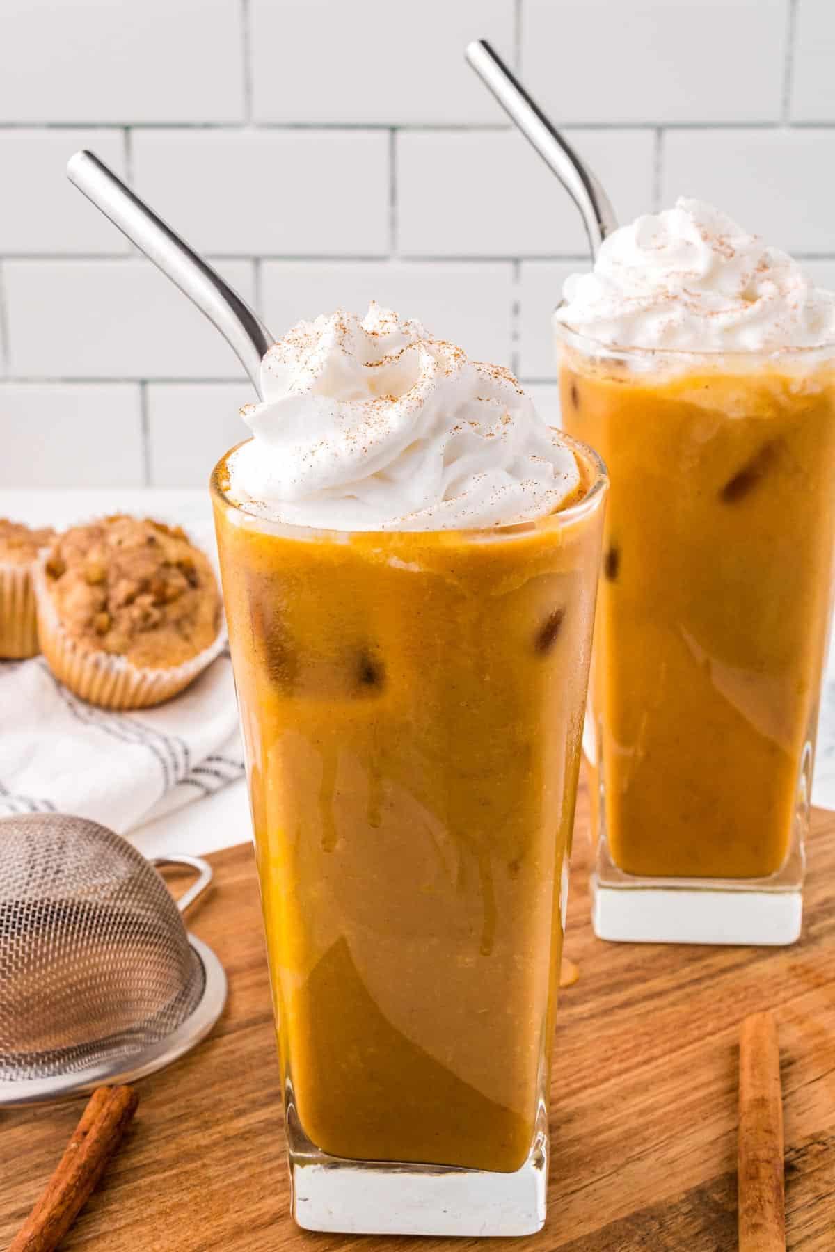 A metal straw in each of two glasses of pumpkin coffee drink.
