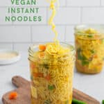 Long noodles being pulled by chopsticks out of a jar of broth and veggies.