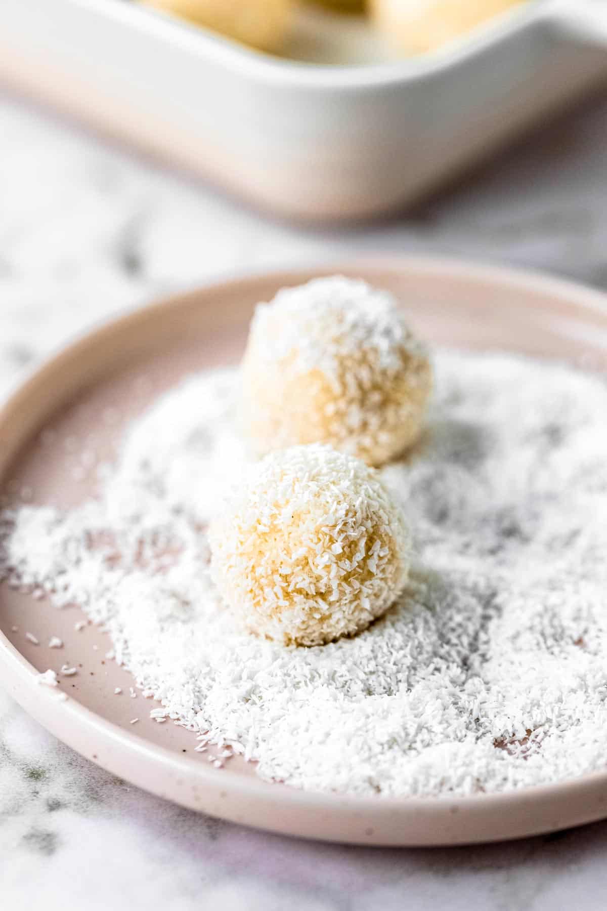 Two bliss balls in a dish of coconut for coating.