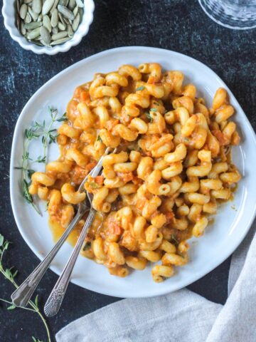 Two forks in a plate of saucy rotini noodles.