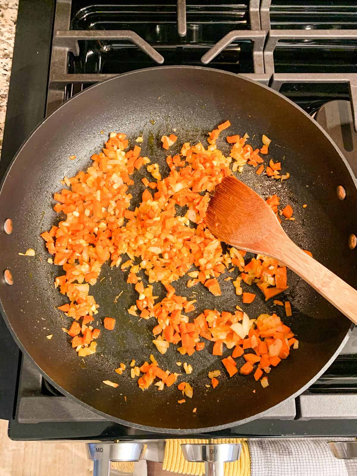 Diced onions and carrots sautéing in a skillet.