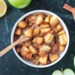 Small wooden spoon scooping up stovetop cinnamon apples from a bowl.