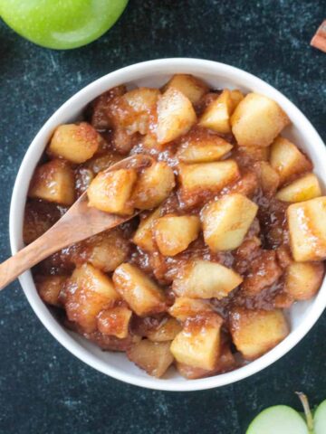 Small wooden spoon scooping up stovetop cinnamon apples from a bowl.